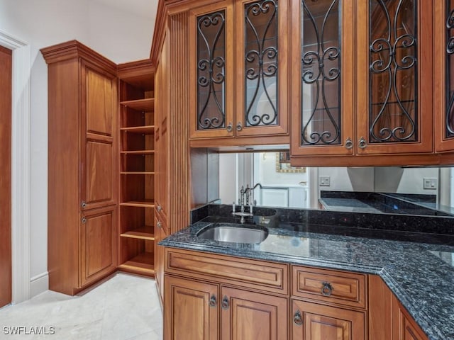 kitchen with dark stone countertops, brown cabinets, glass insert cabinets, and a sink