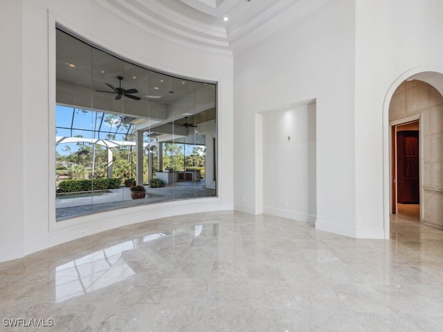 spare room with marble finish floor, arched walkways, a high ceiling, a sunroom, and baseboards