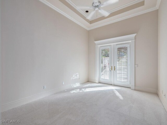 empty room with a tray ceiling, french doors, carpet floors, and ornamental molding