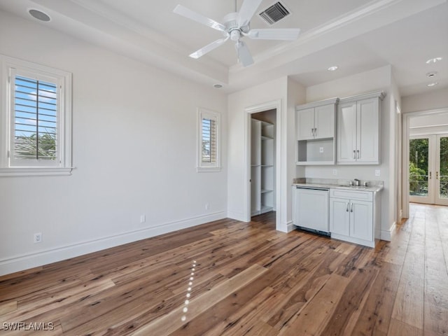 kitchen featuring visible vents, baseboards, paneled dishwasher, a raised ceiling, and wood-type flooring