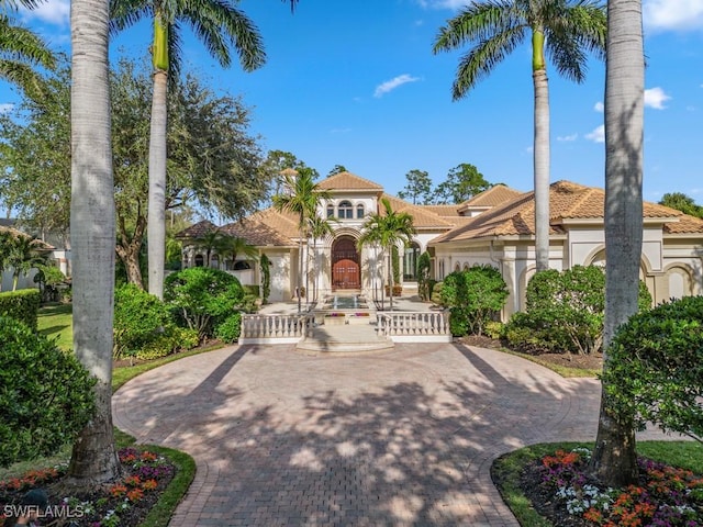 mediterranean / spanish-style house featuring stucco siding, a tile roof, and decorative driveway