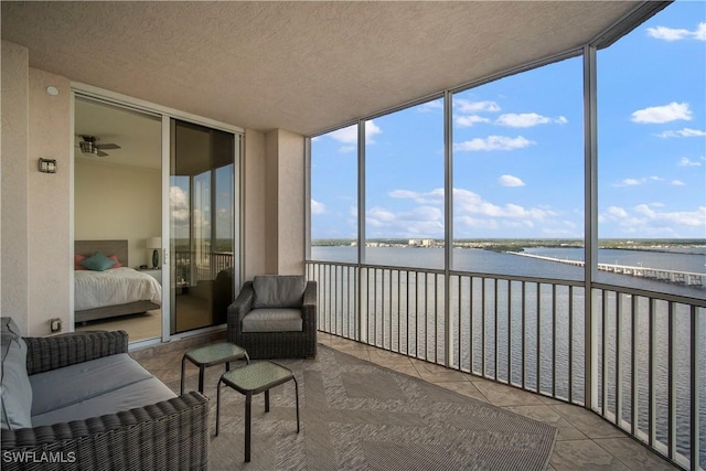 sunroom featuring ceiling fan and a water view