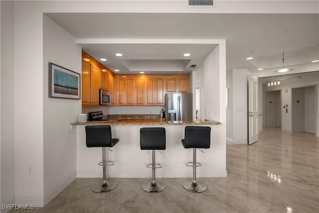 kitchen with a breakfast bar, light stone counters, and stainless steel appliances