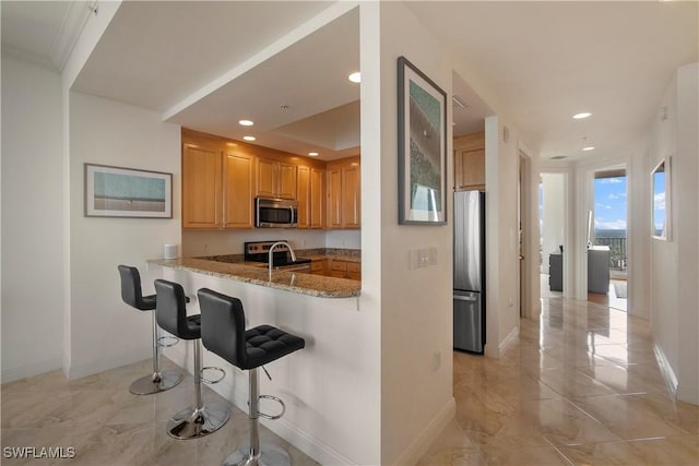 kitchen featuring sink, a breakfast bar area, light stone countertops, kitchen peninsula, and stainless steel appliances