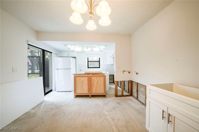 kitchen with pendant lighting, white cabinetry, white fridge, and a notable chandelier