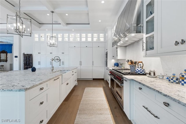 kitchen featuring sink, wall chimney range hood, white cabinets, and decorative light fixtures