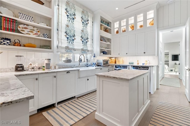 kitchen featuring sink, built in features, a center island, light stone counters, and white cabinets