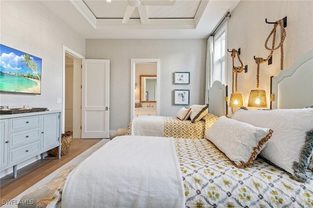 bedroom featuring a raised ceiling, ensuite bathroom, and light hardwood / wood-style floors