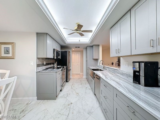 kitchen with marble finish floor, gray cabinetry, a sink, a tray ceiling, and stainless steel appliances