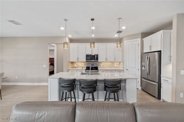 kitchen featuring a breakfast bar area, stainless steel appliances, light countertops, backsplash, and white cabinets