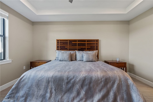 bedroom with light hardwood / wood-style flooring, a raised ceiling, and ceiling fan