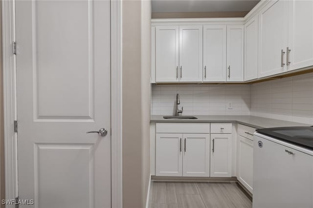 kitchen with dishwashing machine, stove, a sink, white cabinets, and backsplash