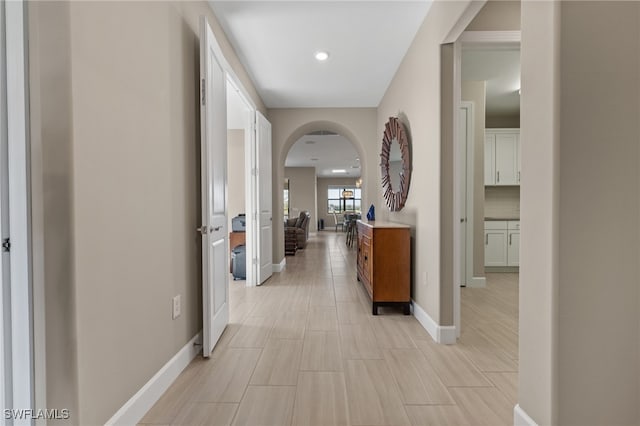 corridor with arched walkways, recessed lighting, and baseboards