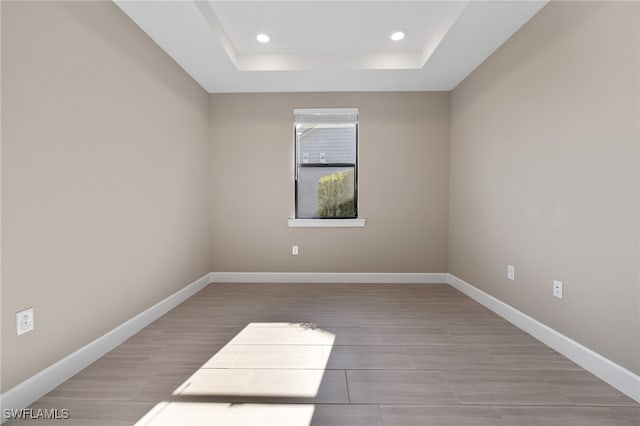 unfurnished room with recessed lighting, a raised ceiling, and baseboards