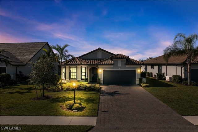 mediterranean / spanish home featuring an attached garage, a front lawn, decorative driveway, and stucco siding