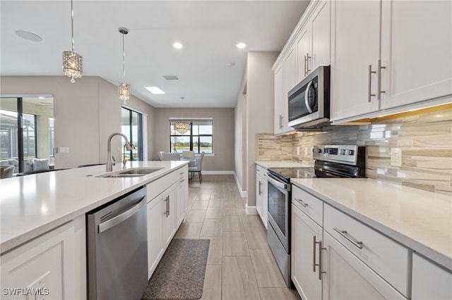 kitchen with backsplash, white cabinets, hanging light fixtures, sink, and appliances with stainless steel finishes