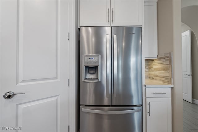 kitchen with arched walkways, white cabinetry, stainless steel fridge with ice dispenser, light countertops, and decorative backsplash