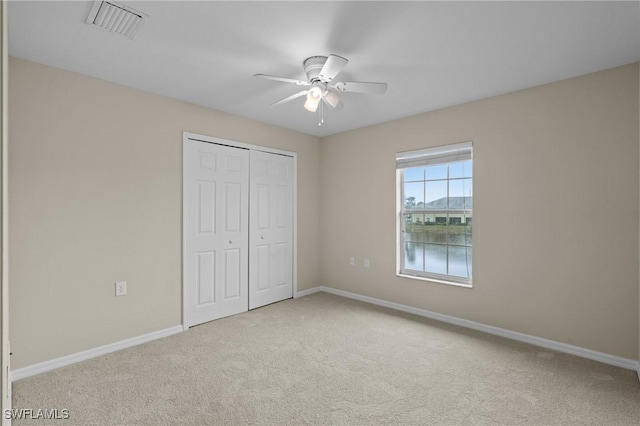 unfurnished bedroom with visible vents, a closet, carpet floors, baseboards, and ceiling fan