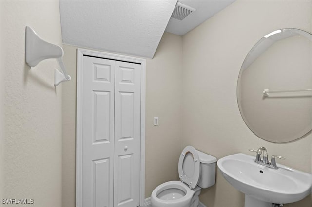 half bathroom with toilet, visible vents, a closet, and a sink