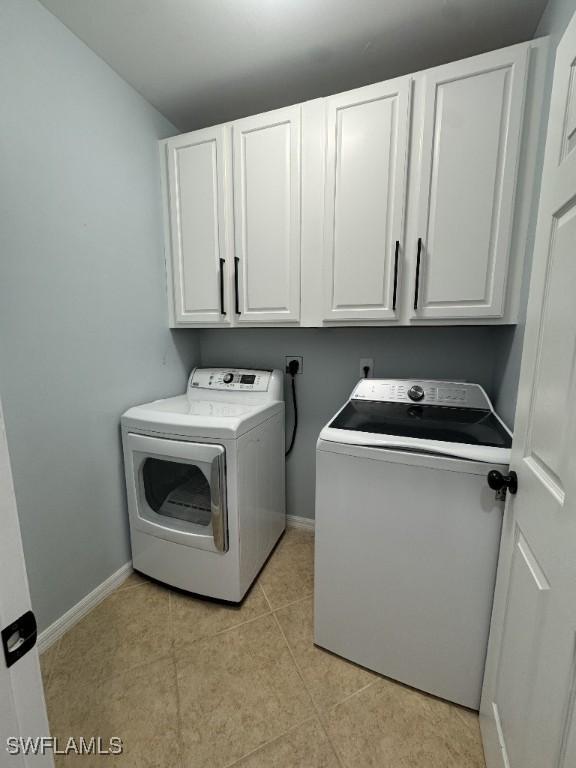 laundry area featuring washing machine and dryer, light tile patterned floors, and cabinets