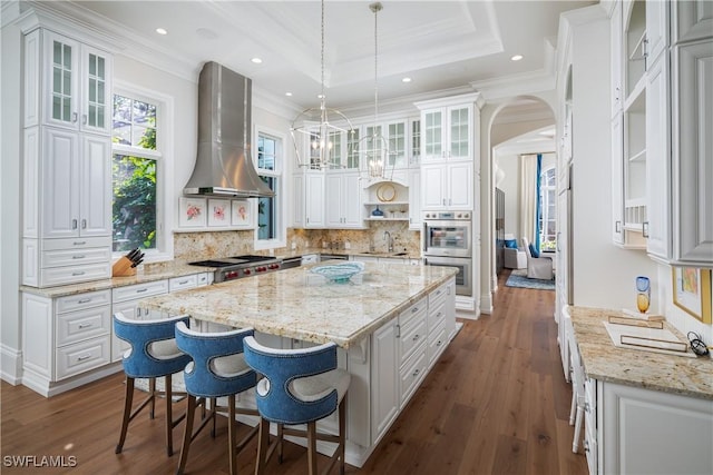 kitchen featuring a raised ceiling, exhaust hood, pendant lighting, a center island, and white cabinetry