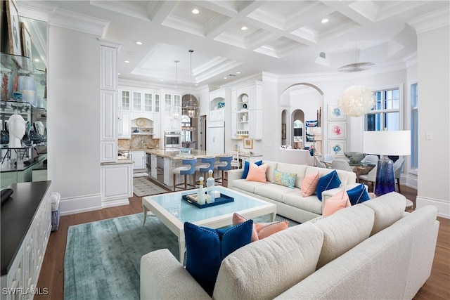 living room featuring dark wood-type flooring, coffered ceiling, ornamental molding, beamed ceiling, and a notable chandelier