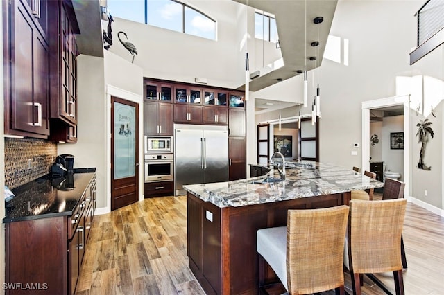 kitchen featuring sink, built in appliances, dark stone countertops, a towering ceiling, and a kitchen island with sink