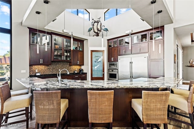 kitchen featuring sink, backsplash, built in appliances, a large island with sink, and pendant lighting