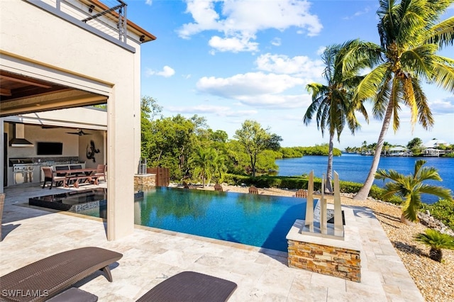 view of pool featuring a patio, a water view, ceiling fan, and exterior kitchen