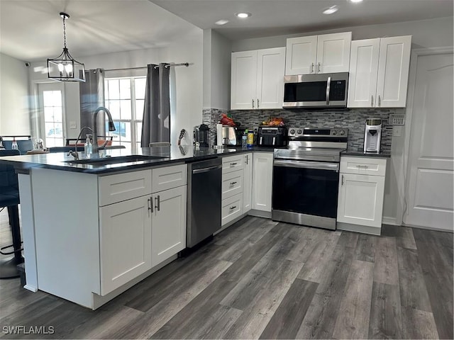 kitchen featuring sink, kitchen peninsula, pendant lighting, white cabinets, and appliances with stainless steel finishes