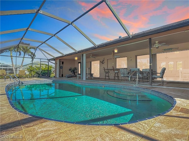 pool at dusk with ceiling fan, a patio, and glass enclosure