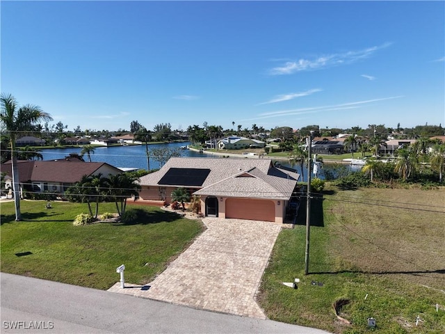 ranch-style home with solar panels, a garage, a water view, and a front yard