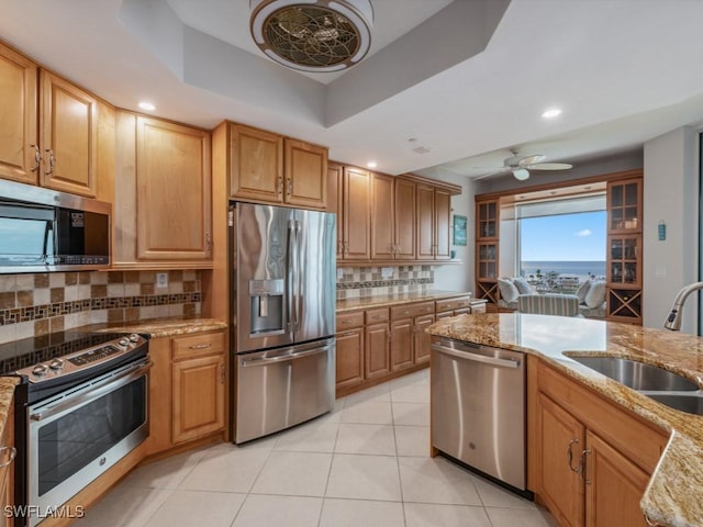 kitchen featuring light stone countertops, sink, stainless steel appliances, a raised ceiling, and backsplash