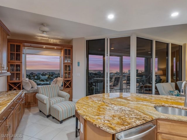 kitchen with light tile patterned flooring, light stone counters, stainless steel dishwasher, and sink