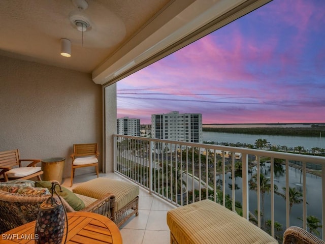 balcony at dusk featuring ceiling fan and a water view