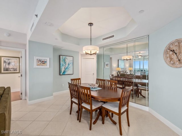 tiled dining area with a raised ceiling and a chandelier