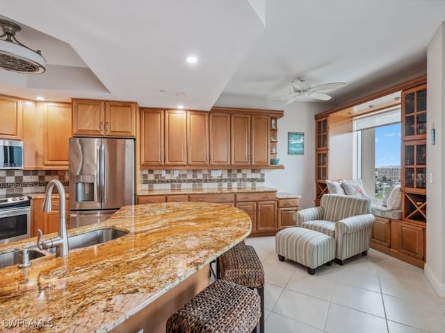 kitchen with sink, appliances with stainless steel finishes, tasteful backsplash, light stone counters, and a breakfast bar area