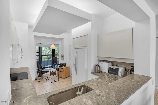 kitchen featuring white refrigerator with ice dispenser, hanging light fixtures, light stone countertops, light tile patterned floors, and black electric cooktop