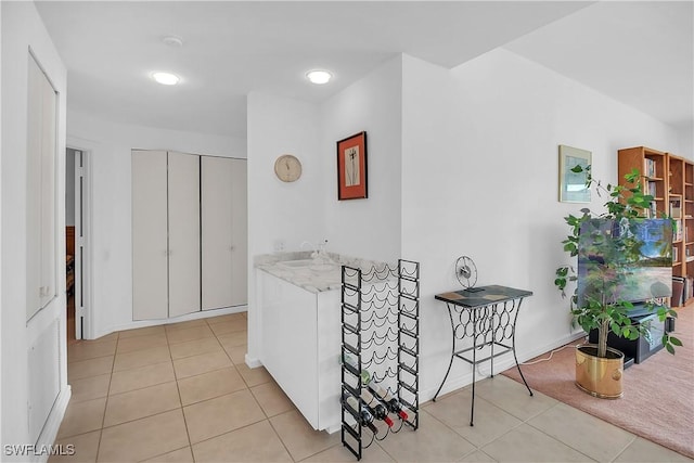 kitchen featuring white cabinets, light stone countertops, light tile patterned floors, and sink