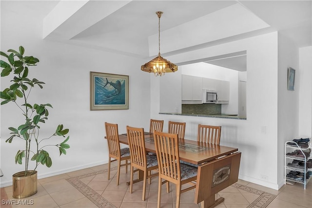 tiled dining space with a chandelier and a raised ceiling