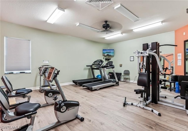 exercise room with ceiling fan, a textured ceiling, and light wood-type flooring