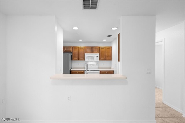 kitchen with light tile patterned floors, kitchen peninsula, stainless steel refrigerator, and range