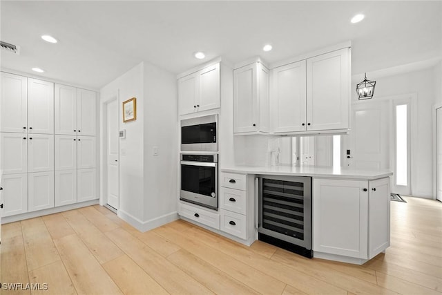 kitchen with recessed lighting, beverage cooler, stainless steel appliances, white cabinets, and light wood-style floors