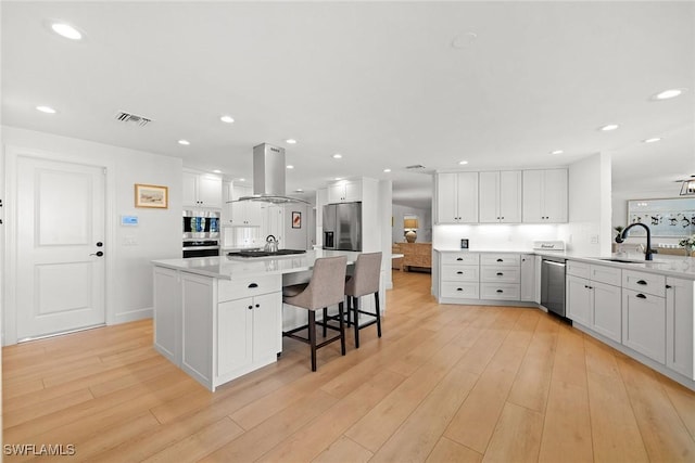 kitchen featuring island range hood, stainless steel appliances, a sink, visible vents, and light wood-type flooring