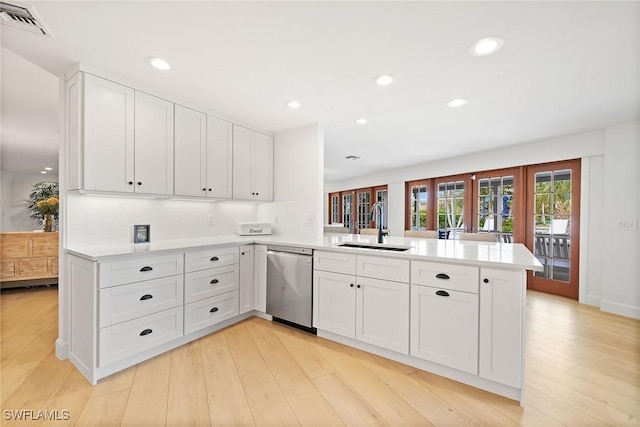 kitchen featuring light wood-style flooring, a peninsula, a sink, light countertops, and stainless steel dishwasher