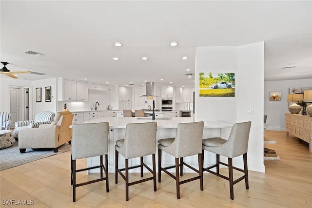 kitchen featuring a breakfast bar, white cabinets, open floor plan, light countertops, and light wood-type flooring