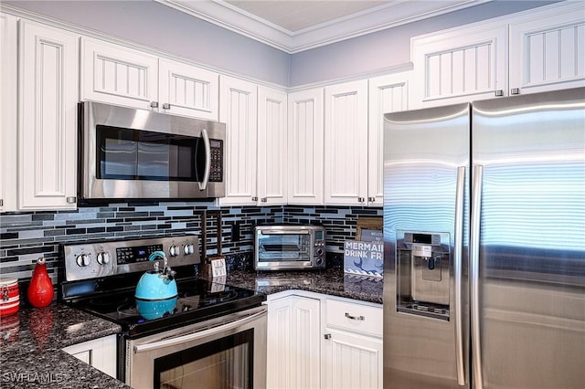 kitchen featuring white cabinetry, stainless steel appliances, dark stone counters, and ornamental molding