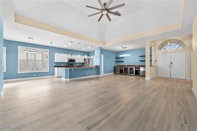 unfurnished living room featuring a tray ceiling, ceiling fan, a towering ceiling, and light wood-type flooring