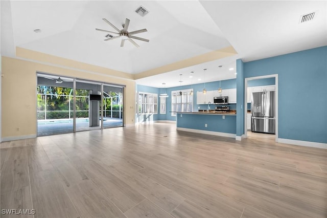 unfurnished living room featuring a tray ceiling, light hardwood / wood-style flooring, ceiling fan, and sink