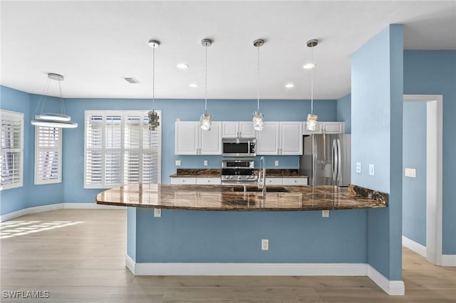 kitchen featuring dark stone counters, stainless steel appliances, sink, decorative light fixtures, and white cabinetry